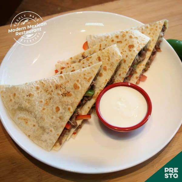 Four triangular quesadilla slices filled with meat and vegetables, served with a side of sour cream.