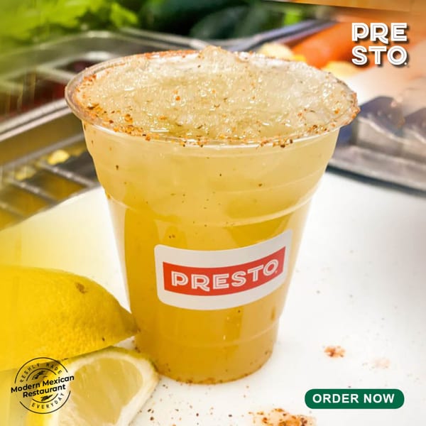 A Presto Fresh Cafe Mexican drink with a spiced rim and lemon wedges on a white surface.